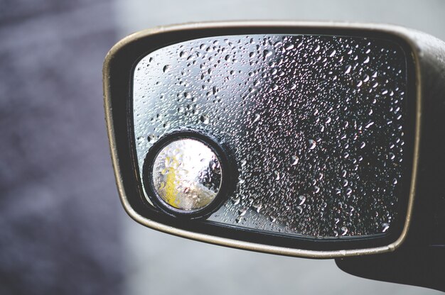 Gros plan d'un rétroviseur couvert de gouttes de pluie sous la lumière du soleil