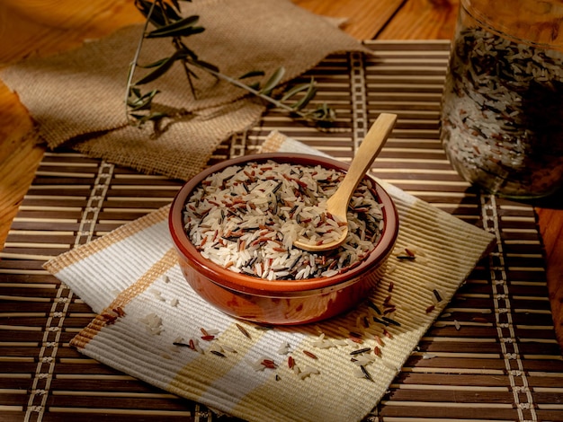 Gros plan de riz sauvage à grain long dans une assiette avec une cuillère en bois sur un morceau de couverture de table