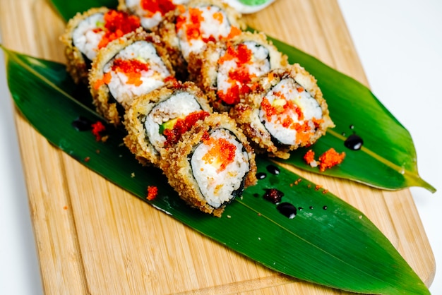 Gros plan de rouleaux de sushi garnis de tobiko rouge servi sur des feuilles