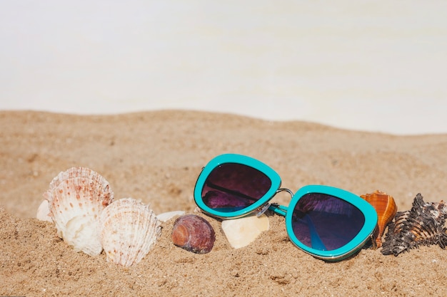 Gros plan de sable avec des lunettes de soleil et des coquillages