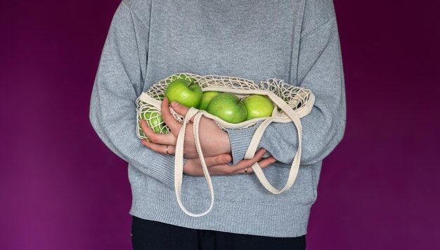 Gros plan sur un sac à cordes avec des pommes vertes dans des mains féminines sur fond violet