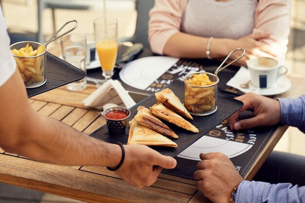 Gros plan sur un serveur méconnaissable servant de la nourriture aux invités pendant l'heure du déjeuner dans un restaurant