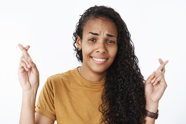 Gros plan d'une sportive afro-américaine nerveuse, incertaine, priant pour que le rêve se réalise, fronçant les sourcils, inquiète et souriante, excitée en croisant les doigts