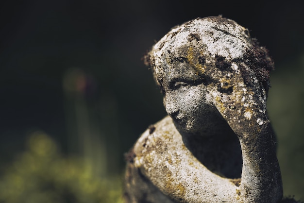 Gros plan d'une statue de pierre moussue rouille d'une femme