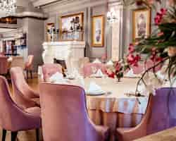 Photo gratuite gros plan d'une table de restaurant avec des chaises en velours rose dans un hall peint en gris avec des peintures classiques