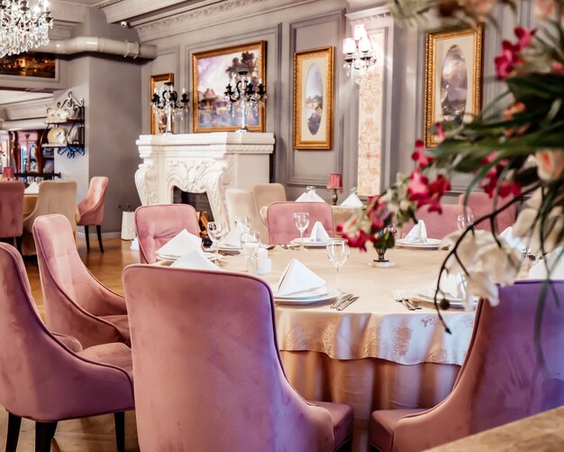 Gros plan d'une table de restaurant avec des chaises en velours rose dans un hall peint en gris avec des peintures classiques