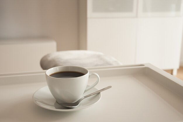 Gros plan d'une tasse de café chaud avec une soucoupe et une cuillère sur un plateau sur le lit le matin