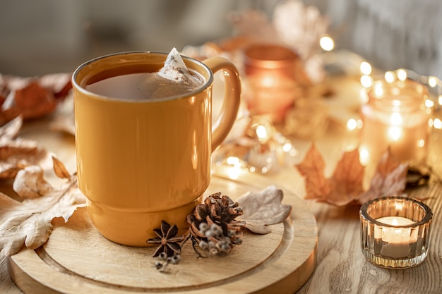 Gros plan d'une tasse de thé parmi les feuilles d'automne et les bougies sur un arrière-plan flou.