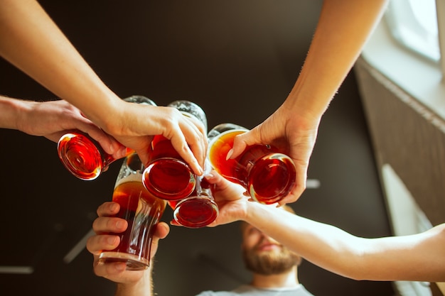 Gros plan tintant. Jeune groupe d'amis buvant de la bière, s'amusant, riant et célébrant ensemble.