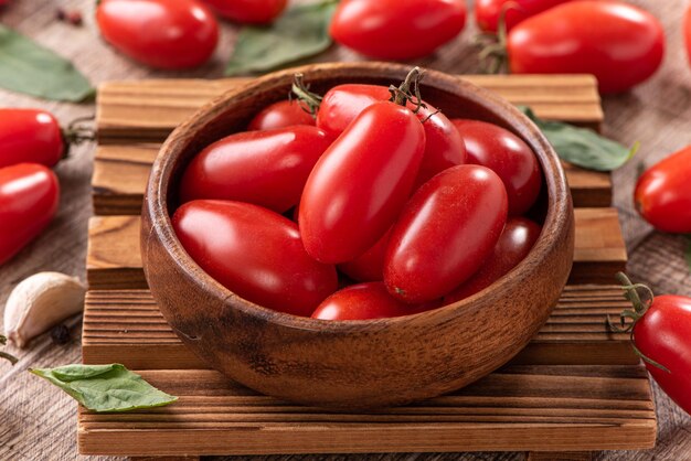 Gros plan de tomates cerises fraîches dans un panier avec des épices sur fond de table en bois.