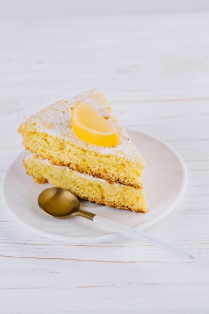 Gros plan d&#39;une tranche de gâteau au citron décorée dans une assiette blanche avec une cuillère