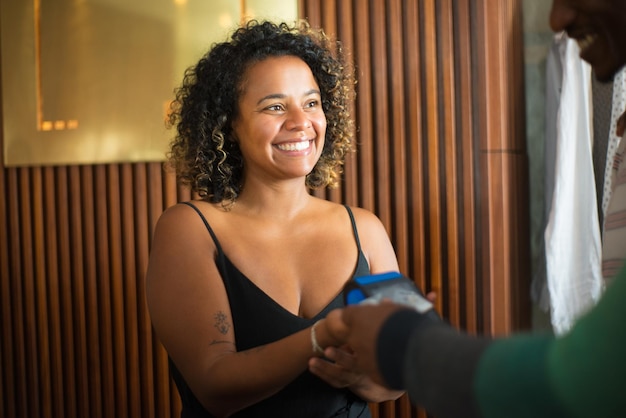 Gros plan d'une vendeuse souriante au magasin de vêtements. Jeune femme tenant un lecteur de carte de crédit en attente de paiement en regardant les acheteurs. Commerce de vêtements, commerce de détail et concept commercial