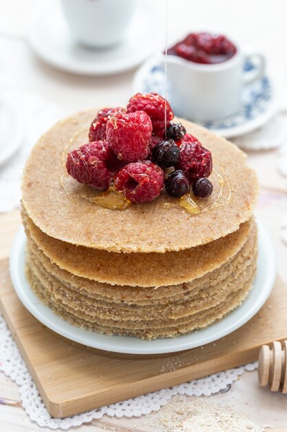 Gros plan vertical à angle élevé de crêpes végétaliennes crues avec du miel et des baies