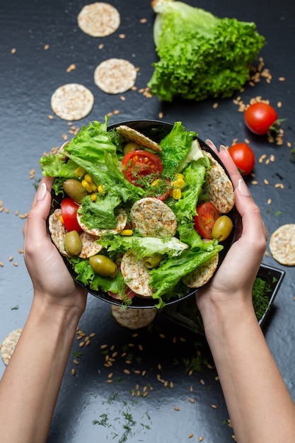 Photo gratuite gros plan vertical d'une personne tenant un bol de salade avec des craquelins et des légumes sous les lumières