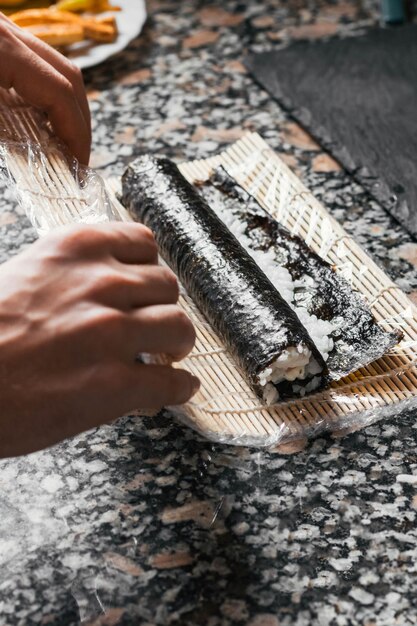 Gros plan vertical d'un processus de fabrication d'un rouleau de sushi sur une table en marbre