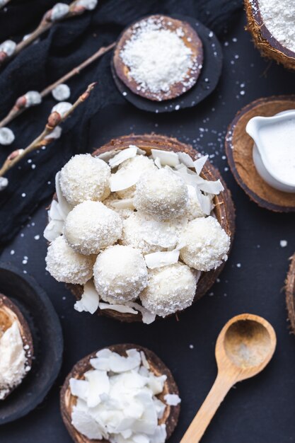 Gros plan vertical de raffaello cru dans un bol en bois avec des morceaux de noix de coco et une cuillère en bois