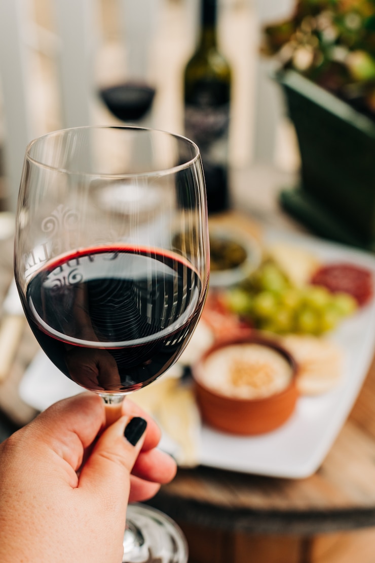 Photo gratuit gros plan vertical sélectif tourné d'une femme tenant un verre de vin rempli de vin rouge foncé