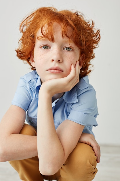 Photo gratuite gros plan vertical shot of funny boy aux cheveux orange et taches de rousseur, tenant la tête avec la main