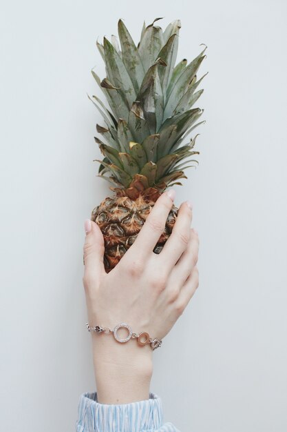 Gros plan vertical tiré d'une main féminine avec un joli bracelet doré tenant un ananas entier