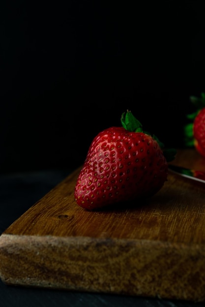 Gros plan vertical tourné de fraises mûres fraîches sur une planche de bois