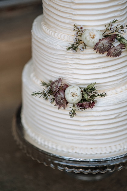 Gros plan vertical tourné d'un gâteau de mariage à trois couches décoré de fleurs sur un plateau d'argent