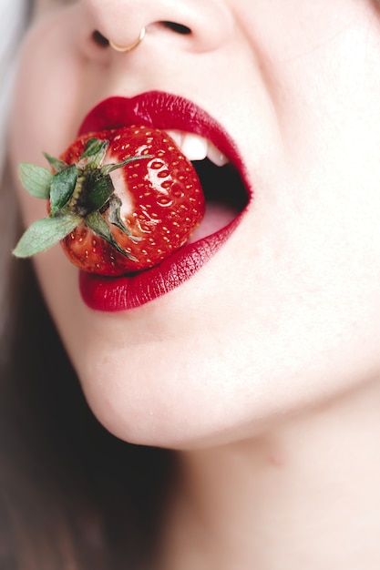 Gros plan vertical tourné d'une jeune femme avec du rouge à lèvres mordant une fraise
