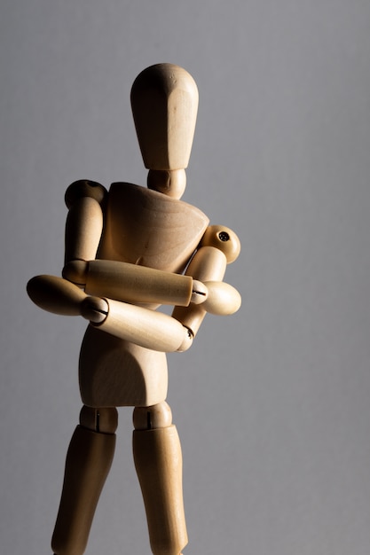 Gros plan vertical tourné d'une poupée de pose en bois avec les bras croisés debout à l'ombre