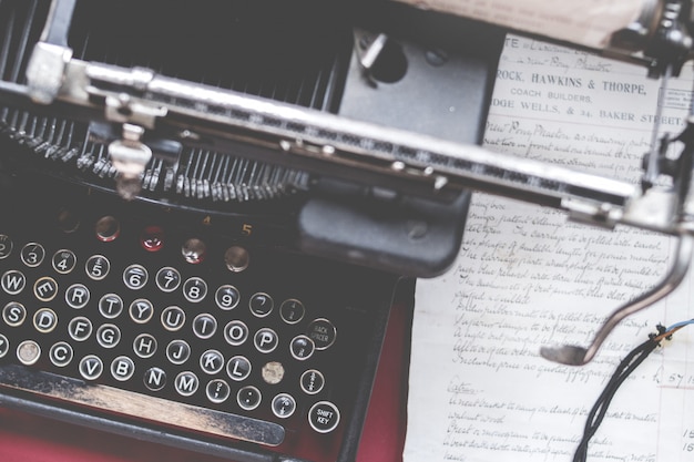 Gros plan d'une vieille machine à écrire vintage sur un bureau rouge avec du papier sur le côté