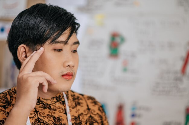 Gros plan sur le visage d'un jeune tailleur asiatique professionnel avec un ruban à mesurer sur le cou pensant en studio.