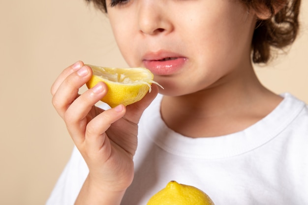 Gros plan, voir un enfant mignon mangeant du citron aigre sur rose