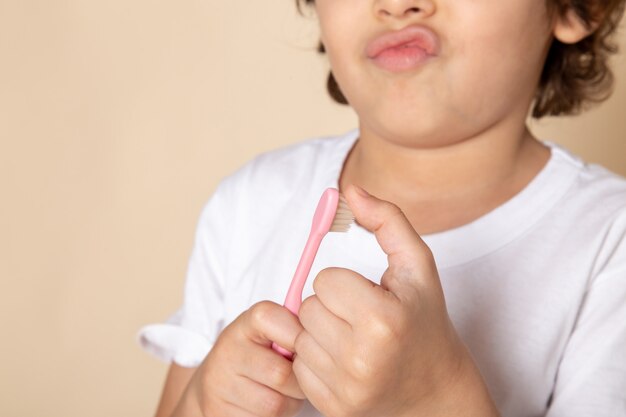 Gros plan, voir un garçon mignon adorable avec une brosse à dents en t-shirt blanc et rose