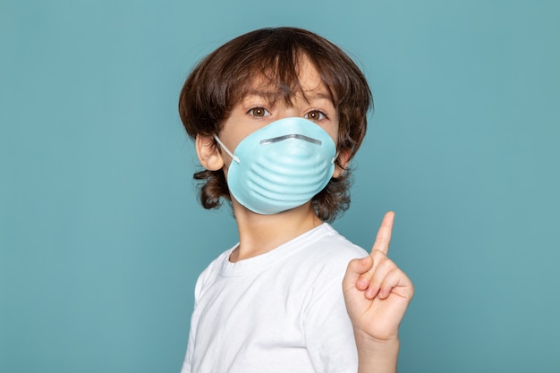 Gros plan, voir mignon petit garçon adorable en bleu masque respiratoire de protection stérile sur t-shirt blanc sur bleu