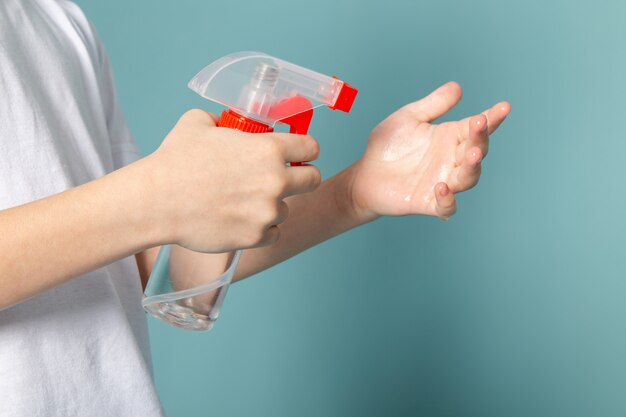 Gros plan, voir le petit garçon à l'aide d'un spray contre le coronavirus en t-shirt blanc sur bleu