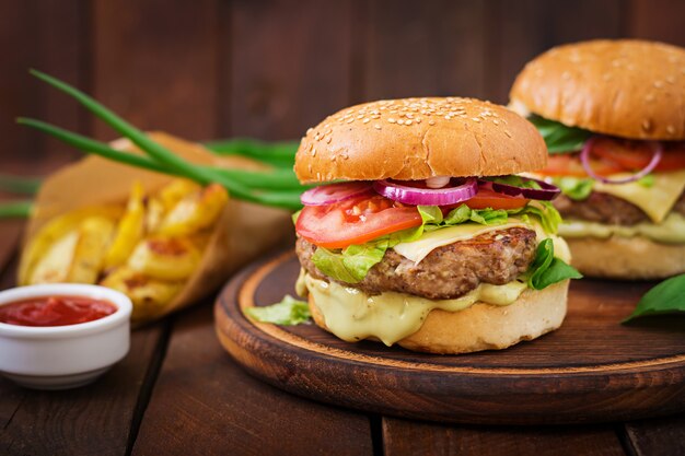Gros sandwich - hamburger avec burger de boeuf juteux, fromage, tomate et oignon rouge sur table en bois