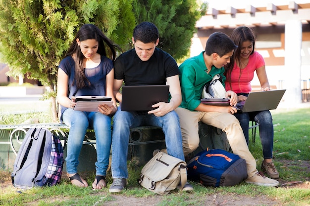 Groupe d'adolescents faisant du réseautage social à l'aide de plusieurs appareils technologiques au lycée