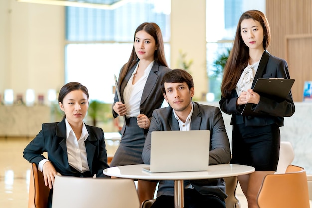 Groupe d'affaires asiatiques intelligentes travail d'équipe uniforme look caméra avec confiance et gaie avec un arrière-plan de bureau de design moderne