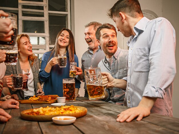 Groupe d'amis appréciant des boissons en soirée avec de la bière sur une table en bois