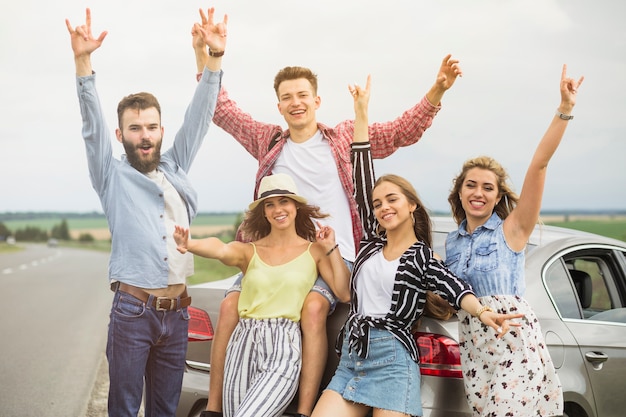 Groupe d&#39;amis debout devant la voiture, levant les mains