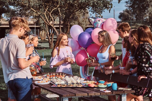 Groupe d'amis heureux s'amusant ensemble pour célébrer un anniversaire au parc extérieur. Des amis disent un toast lors d'une fête de pique-nique en plein air.