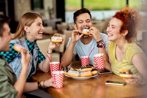 Groupe d'amis joyeux mangeant des beignets dans un café