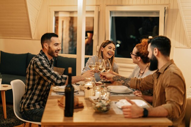 Groupe d'amis joyeux s'amusant tout en dînant et portant un toast avec du vin à la table à manger
