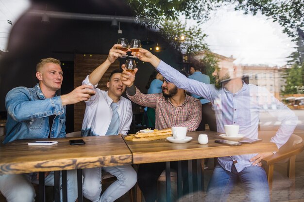 Groupe d&#39;amis masculins soulevant des toasts dans le restaurant