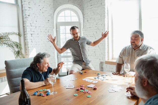 Groupe d'amis matures heureux jouant aux cartes et boire du vin