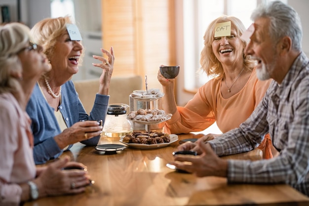 Groupe d'amis matures joyeux avec des autocollants sur le front jouant au jeu de devinettes à la maison L'accent est mis sur la femme avec le mot chat sur une étiquette