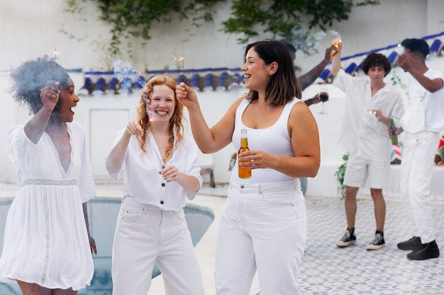 Groupe d'amis s'amusant lors d'une soirée blanche avec boissons au bord de la piscine