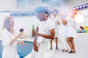 Photo gratuite groupe d'amis s'amusant lors d'une soirée blanche avec boissons au bord de la piscine