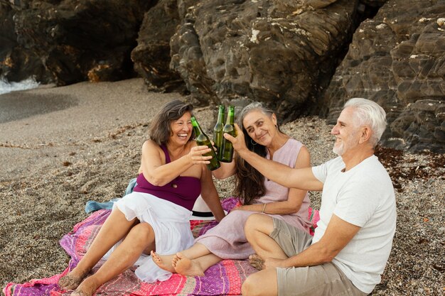 Groupe d'amis seniors applaudissant avec de la bière à la plage