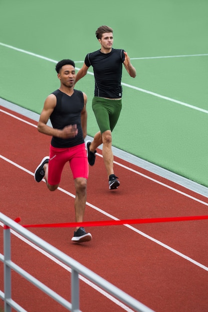 Groupe d'athlètes hommes courir sur une piste de course à l'extérieur