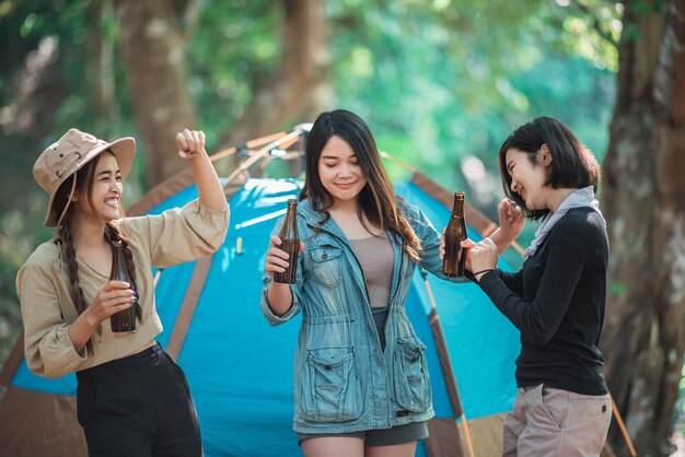 Groupe de belles femmes asiatiques amis voyageurs se détendant devant la tente de camping Ils aiment parler et boire de la bière avec plaisir et heureux ensemble