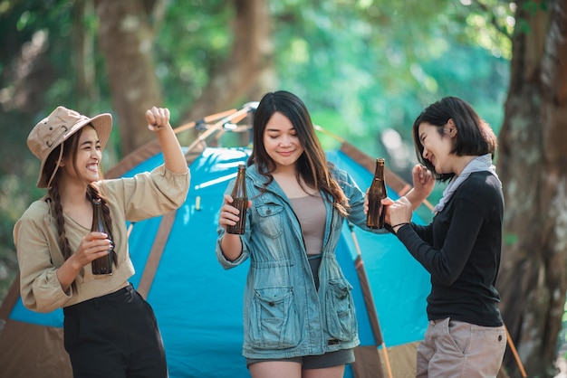 Groupe de belles femmes asiatiques amis voyageurs se détendant devant la tente de camping Ils aiment parler et boire de la bière avec plaisir et heureux ensemble